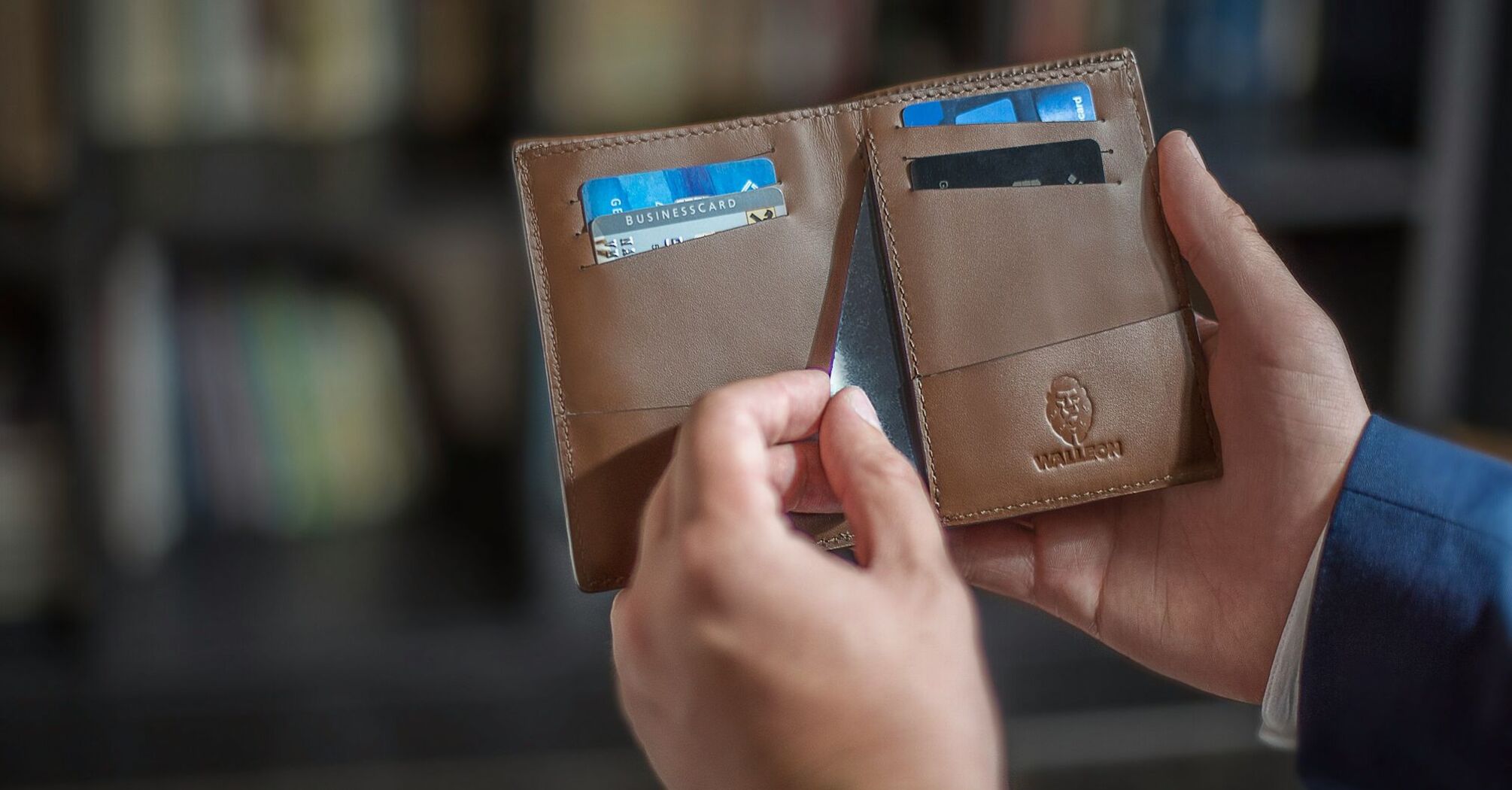 Person holding an open brown leather wallet showing various cards