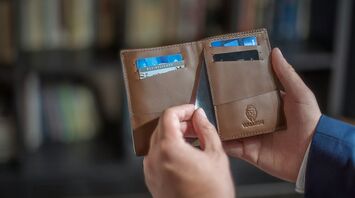 Person holding an open brown leather wallet showing various cards