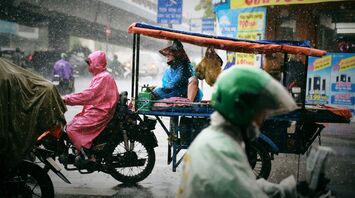 People in raincoats riding through a heavy rainstorm on a city street