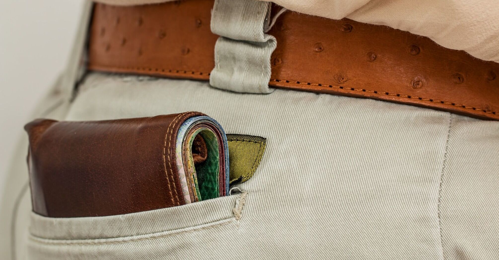 Wallet protruding from the back pocket of beige pants with a leather belt