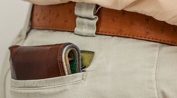 Wallet protruding from the back pocket of beige pants with a leather belt