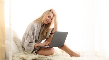 Woman sitting on bed working on laptop