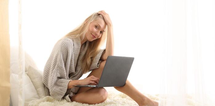 Woman sitting on bed working on laptop