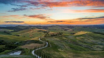 Road between green grass field near mountains under blue and brown sky at golden hour