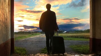 Man with suitcase walking towards a vibrant sunset through an arched tunnel