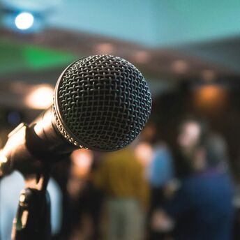 Close-up of a microphone on a stand with a blurred background of people in a room