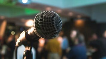 Close-up of a microphone on a stand with a blurred background of people in a room