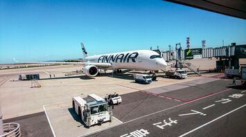 Finnair aircraft docked at an airport gate with ground support equipment and clear blue skies