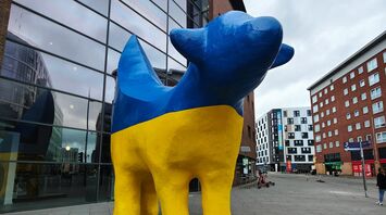A statue of a blue and yellow dog in front of a building