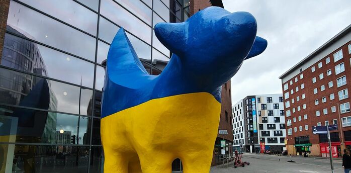 A statue of a blue and yellow dog in front of a building