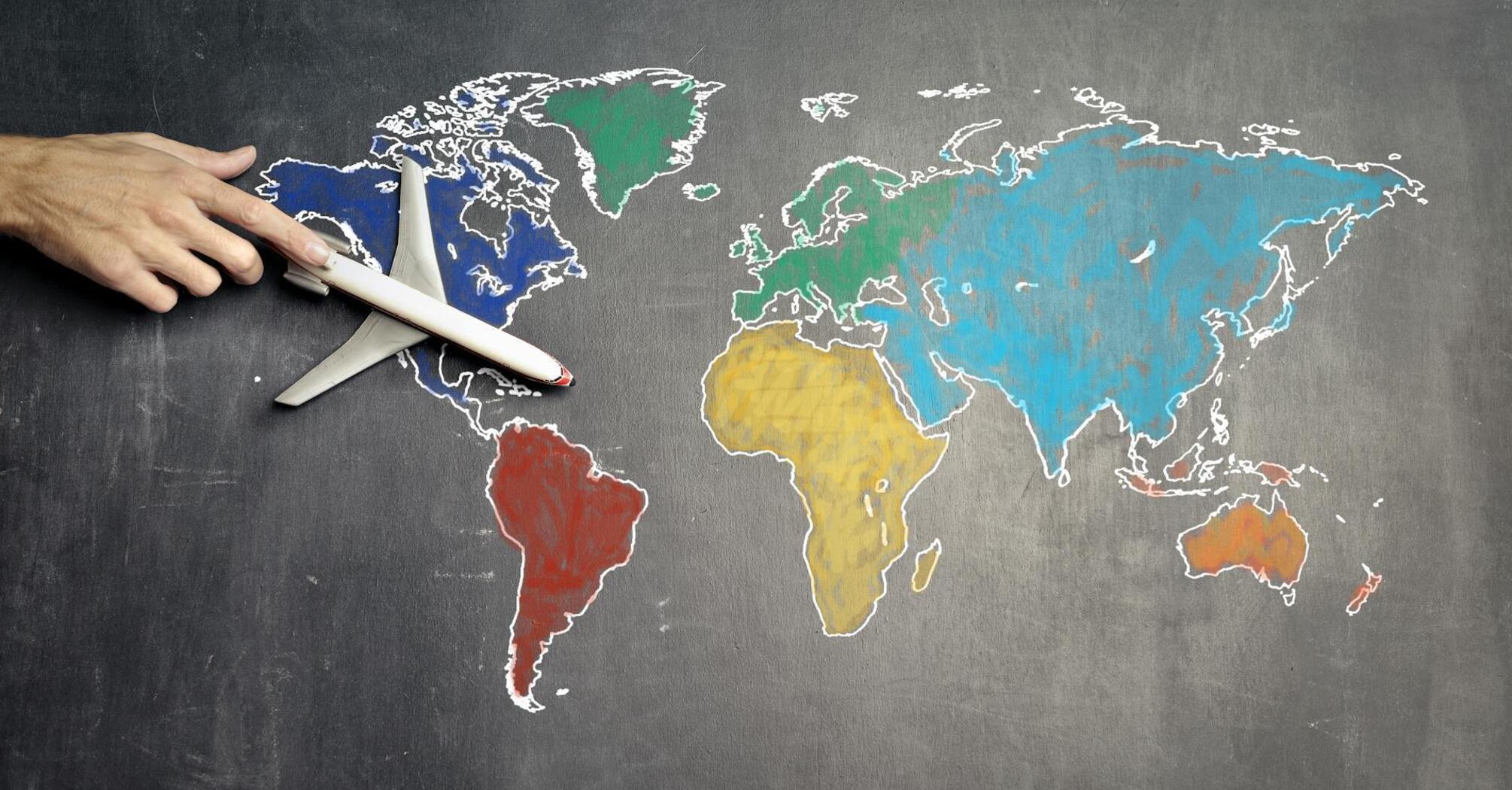A hand positioning a model airplane on a chalk-drawn world map on a blackboard, symbolizing global travel