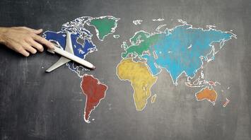 A hand positioning a model airplane on a chalk-drawn world map on a blackboard, symbolizing global travel