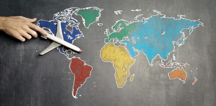 A hand positioning a model airplane on a chalk-drawn world map on a blackboard, symbolizing global travel