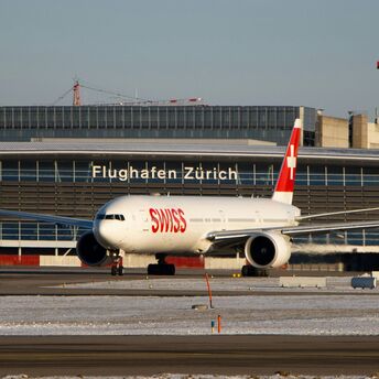 A SWISS airplane on a runway at Zurich Airport, with the airport terminal in the background