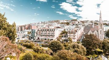 A scenic view of North Devon with residential buildings, a church, and lush greenery under a partly cloudy sky