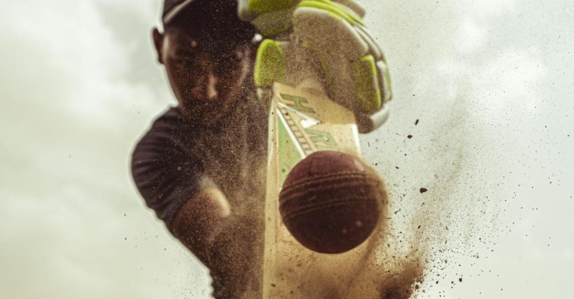 Close-up action shot of a cricket player hitting the ball with a bat