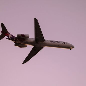 an airplane flying in the air with a pink sky background