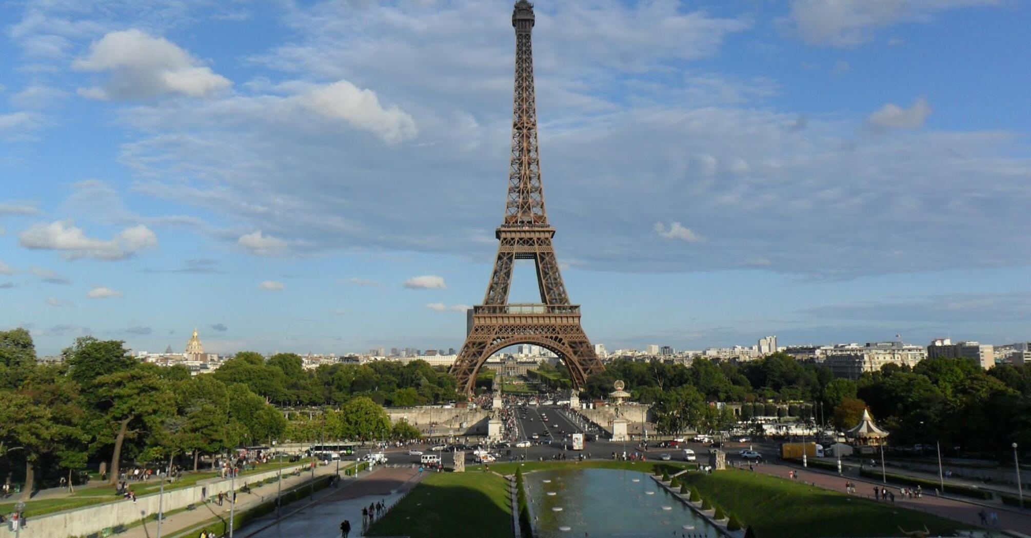 The Eiffel Tower stands tall against a clear blue sky with scattered clouds
