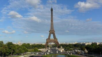 The Eiffel Tower stands tall against a clear blue sky with scattered clouds