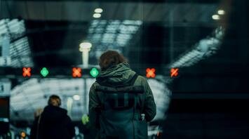 Person standing at a train station gate with digital displays in the background