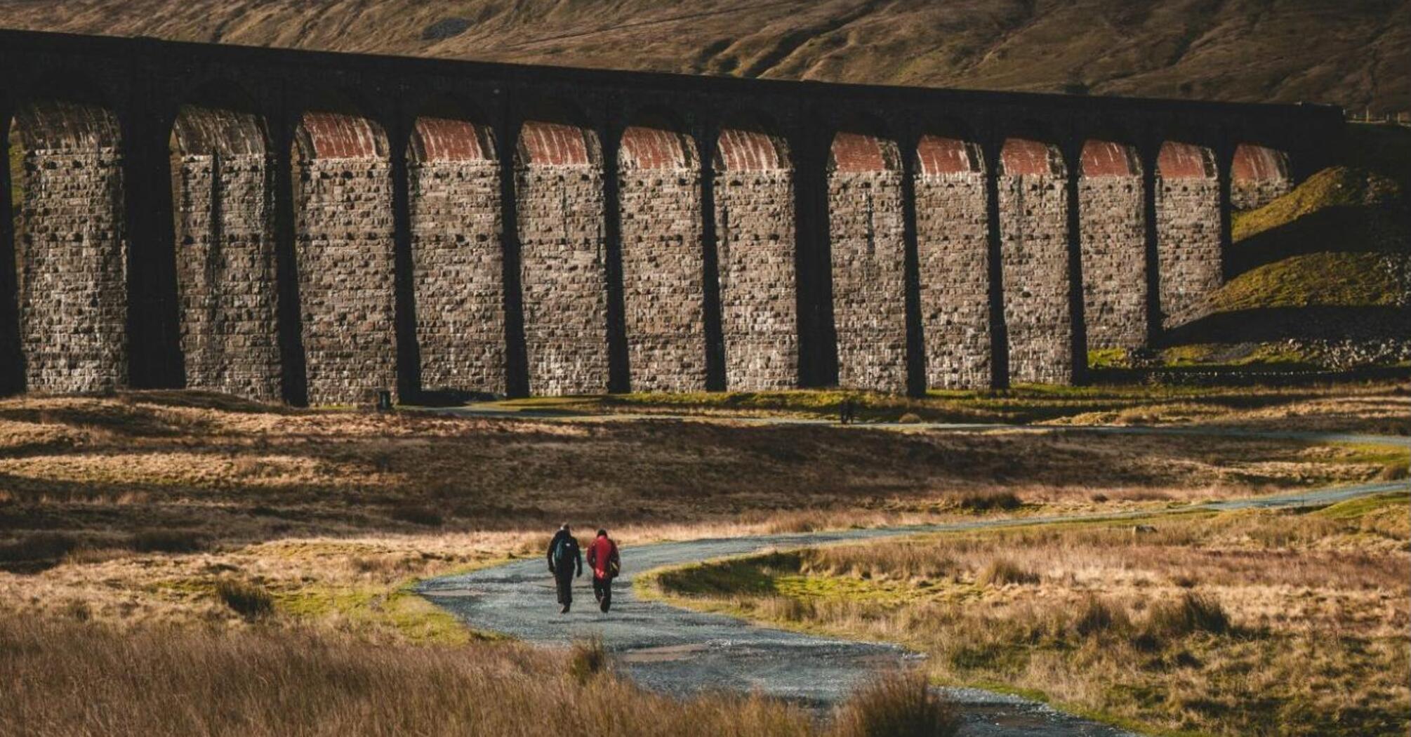 Two cyclists riding on a path beside a historic stone viaduct in the Yorkshire Dales