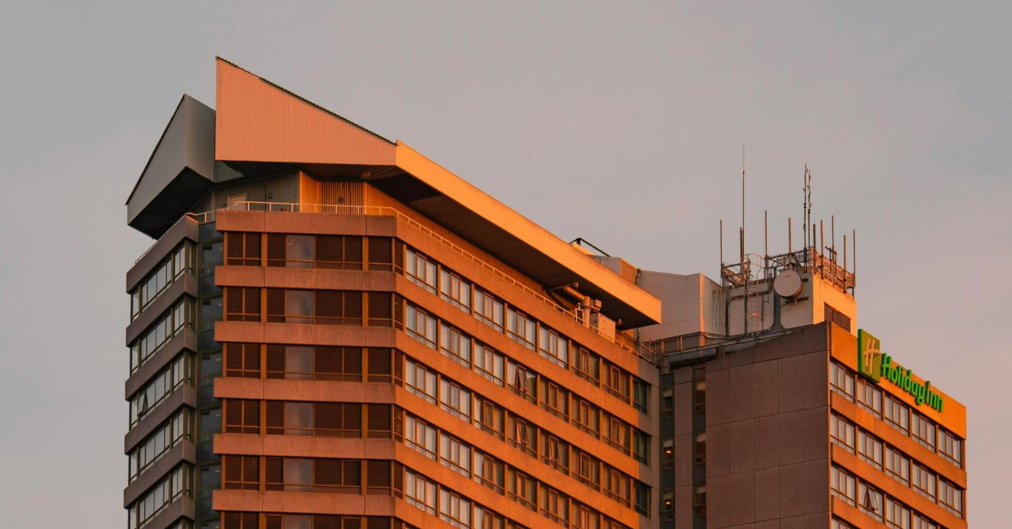 Concrete, modernist, brutalist Holiday Inn Kensington bathed in golden sunset light.