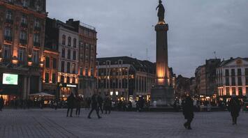Evening view of a busy square in a French city with a tall statue and illuminated buildings