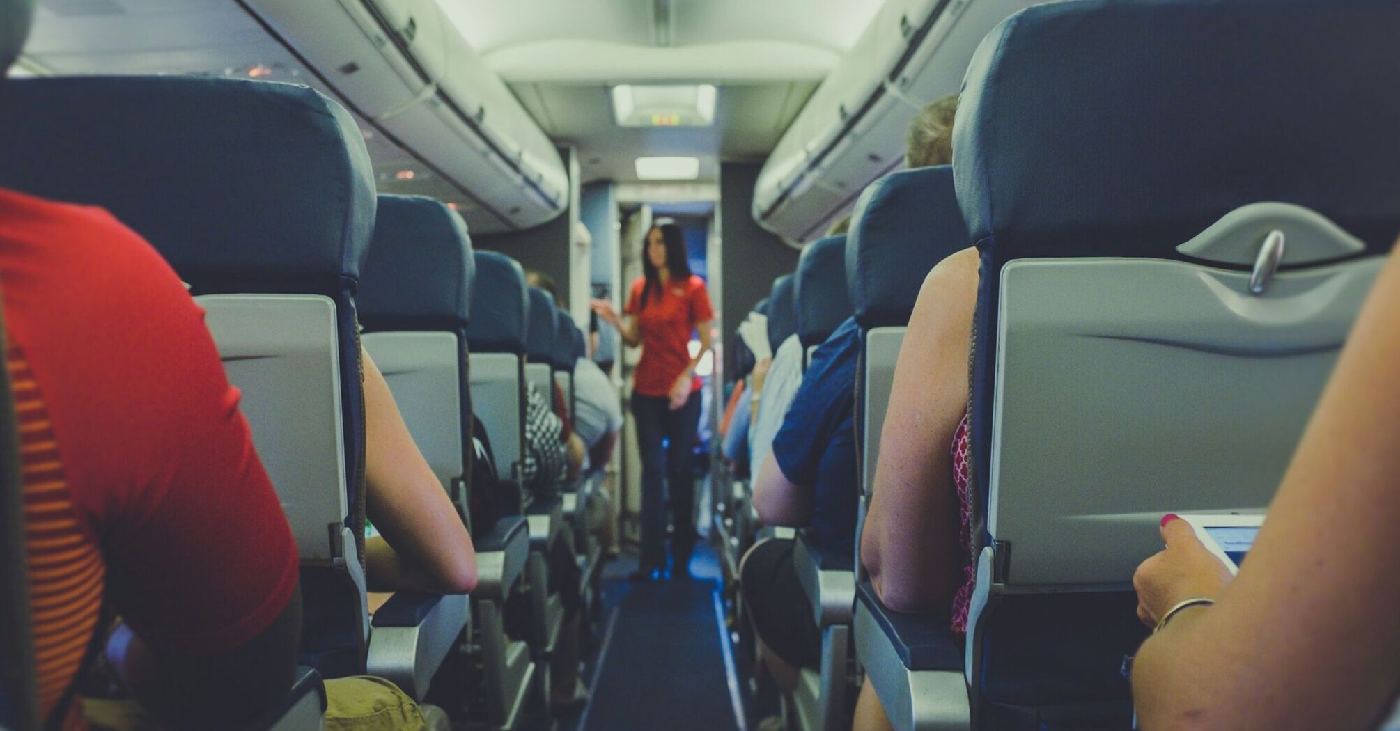 Passengers seated on an airplane with a flight attendant in the aisle