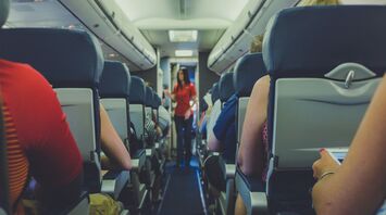 Passengers seated on an airplane with a flight attendant in the aisle