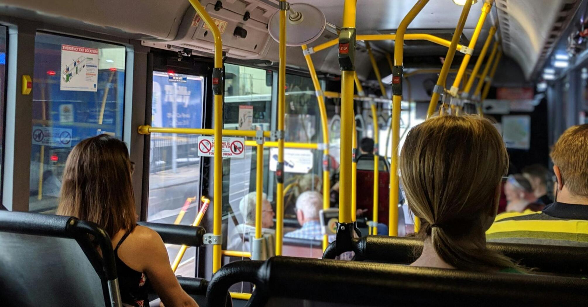 Passengers sitting inside a bus with yellow handrails and windows showing city streets outside