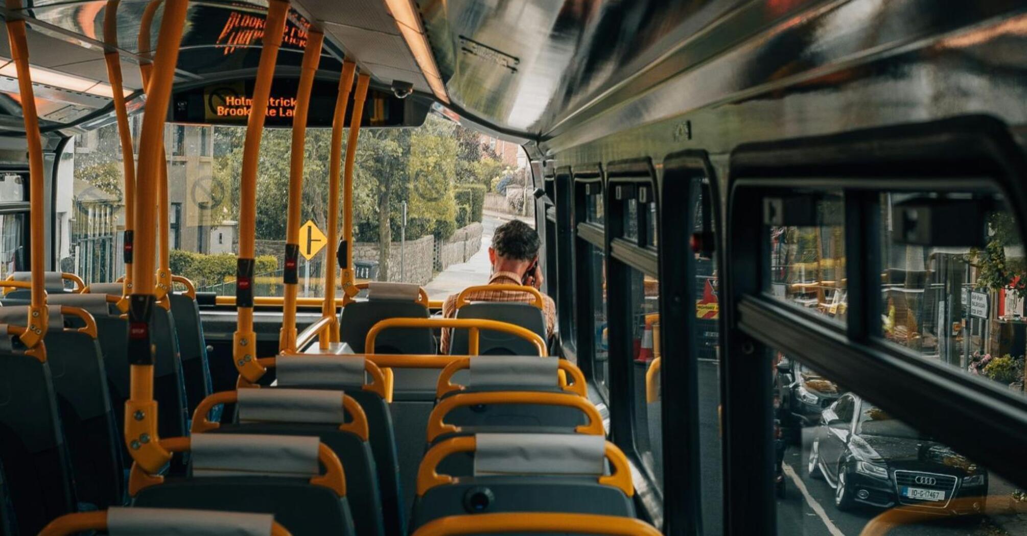 Interior of a bus with empty seats and a passenger in the distance