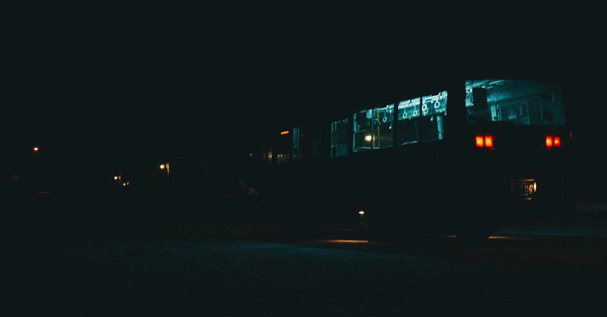 A bus illuminated at night, driving through a dark area with streetlights in the background