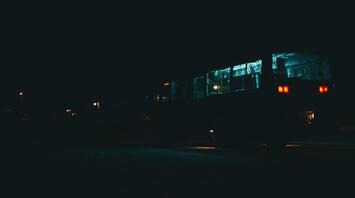 A bus illuminated at night, driving through a dark area with streetlights in the background