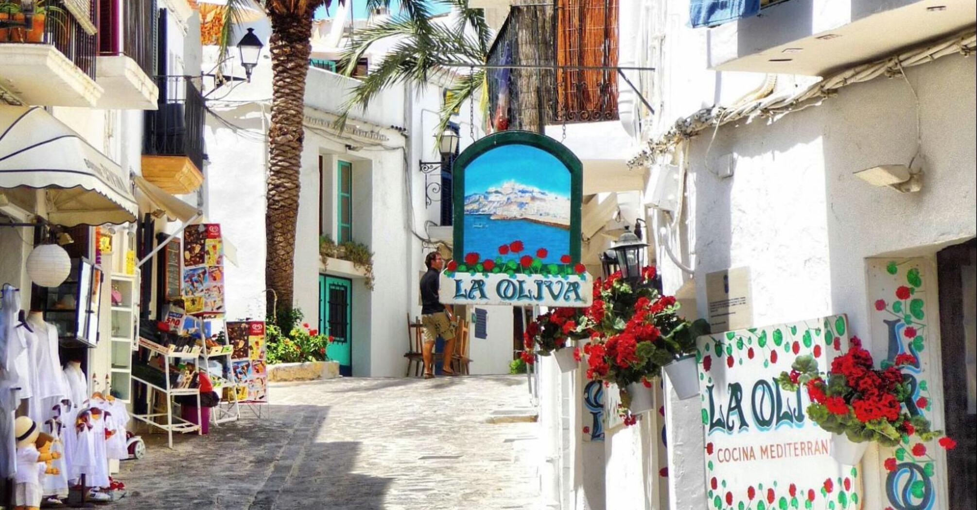 Charming narrow street in Ibiza with whitewashed buildings, colorful storefronts, and vibrant flowers