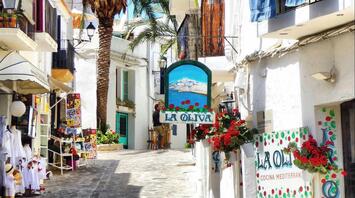 Charming narrow street in Ibiza with whitewashed buildings, colorful storefronts, and vibrant flowers