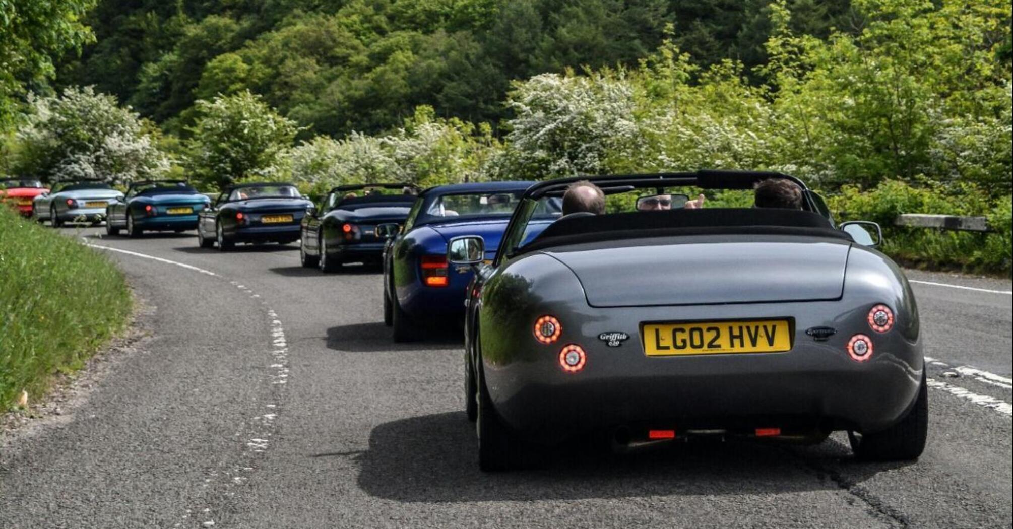 Cars driving on a road through a lush green forest in the Peak District