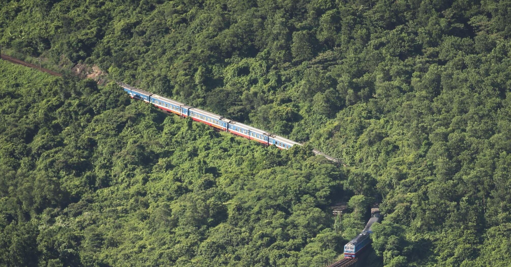 A train on a suspension bridge amidst green mountains