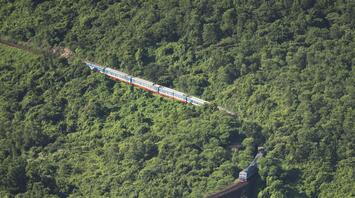 A train on a suspension bridge amidst green mountains
