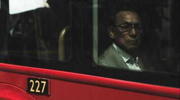 An older man sitting inside a red bus, looking out of the window