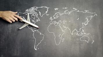 A hand guiding a toy airplane over a world map drawn on a chalkboard