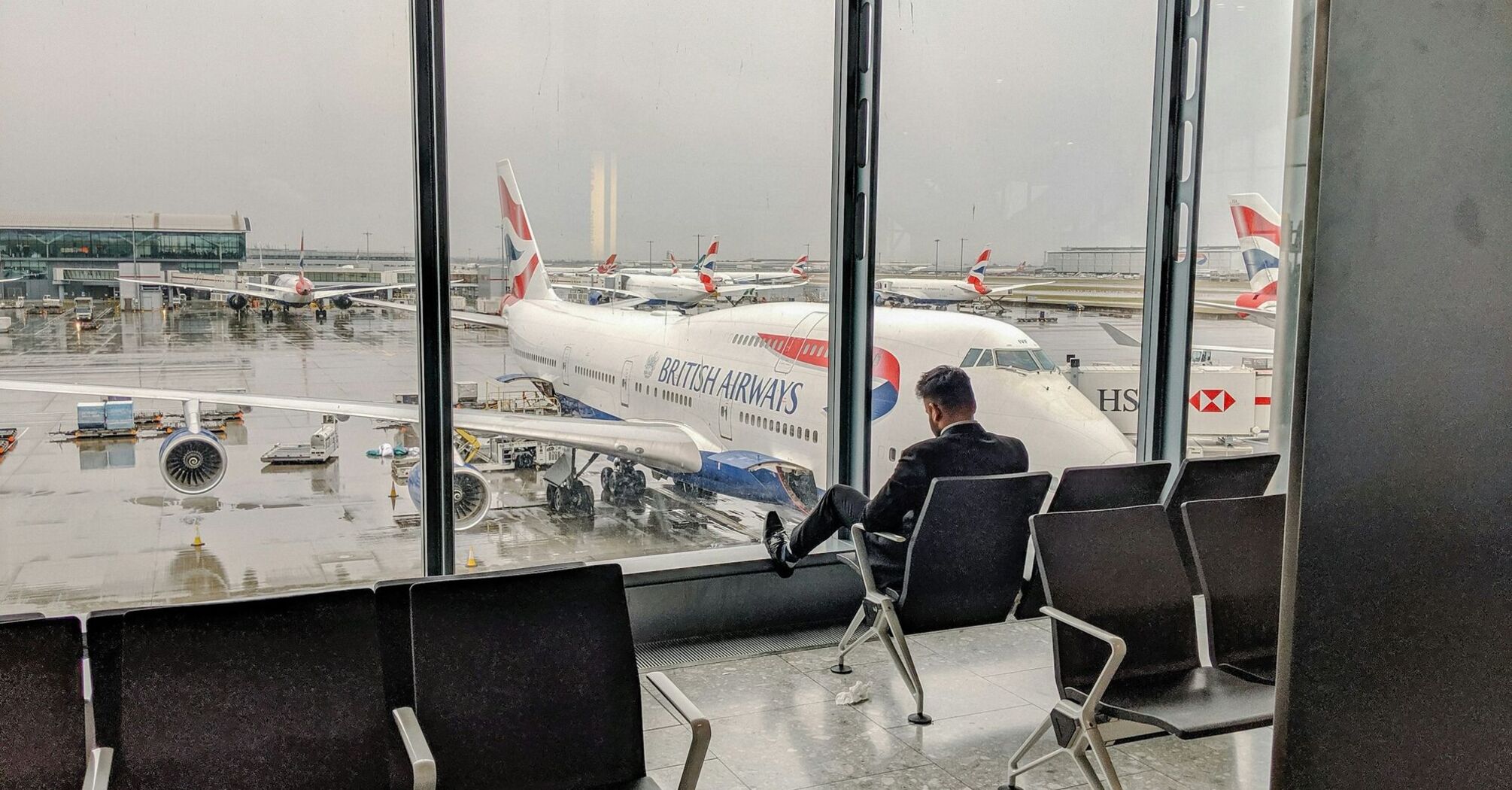 Passenger sitting in airport lounge overlooking British Airways planes