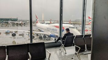 Passenger sitting in airport lounge overlooking British Airways planes