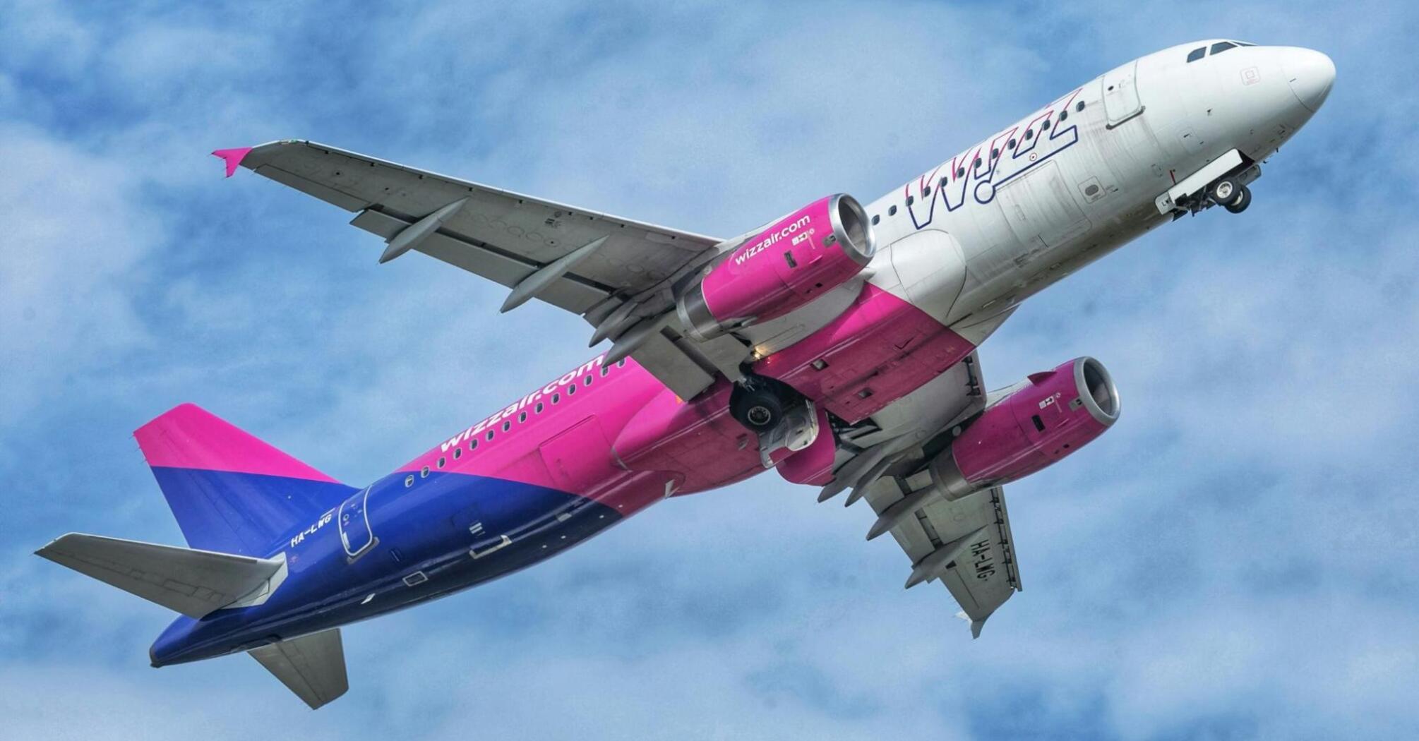 A pink and blue Wizz Air jet airliner in the sky