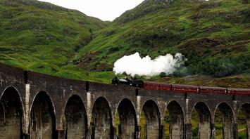 A steam train crossing an old viaduct in a lush green valley