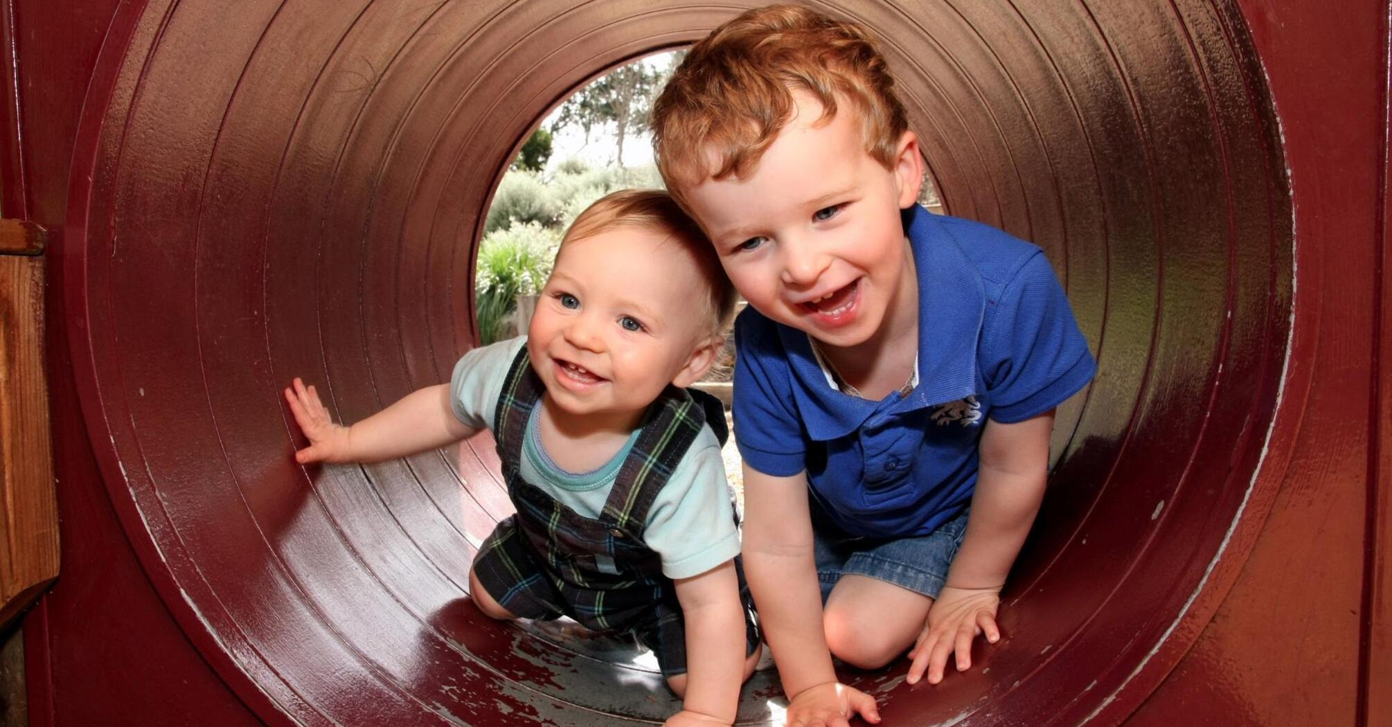 Two little children having fun playing in a tunnel at the playground
