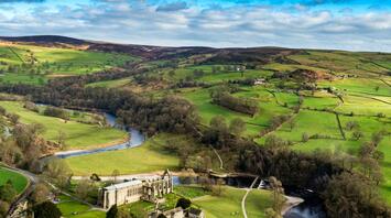 Aerial view of a lush green landscape in the Yorkshire Dales with a historic abbey and a winding river