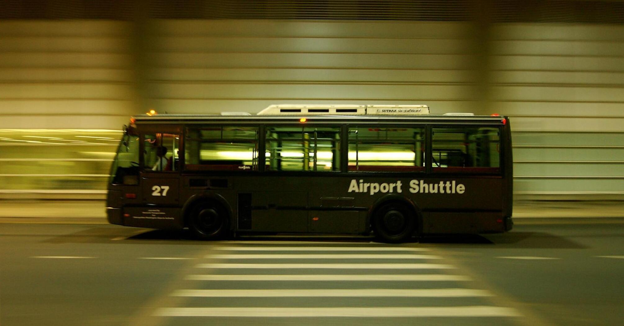 Shuttle bus labeled "Airport Shuttle" in motion at night, crossing a zebra crossing