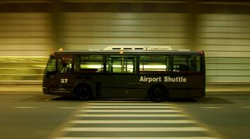 Shuttle bus labeled "Airport Shuttle" in motion at night, crossing a zebra crossing