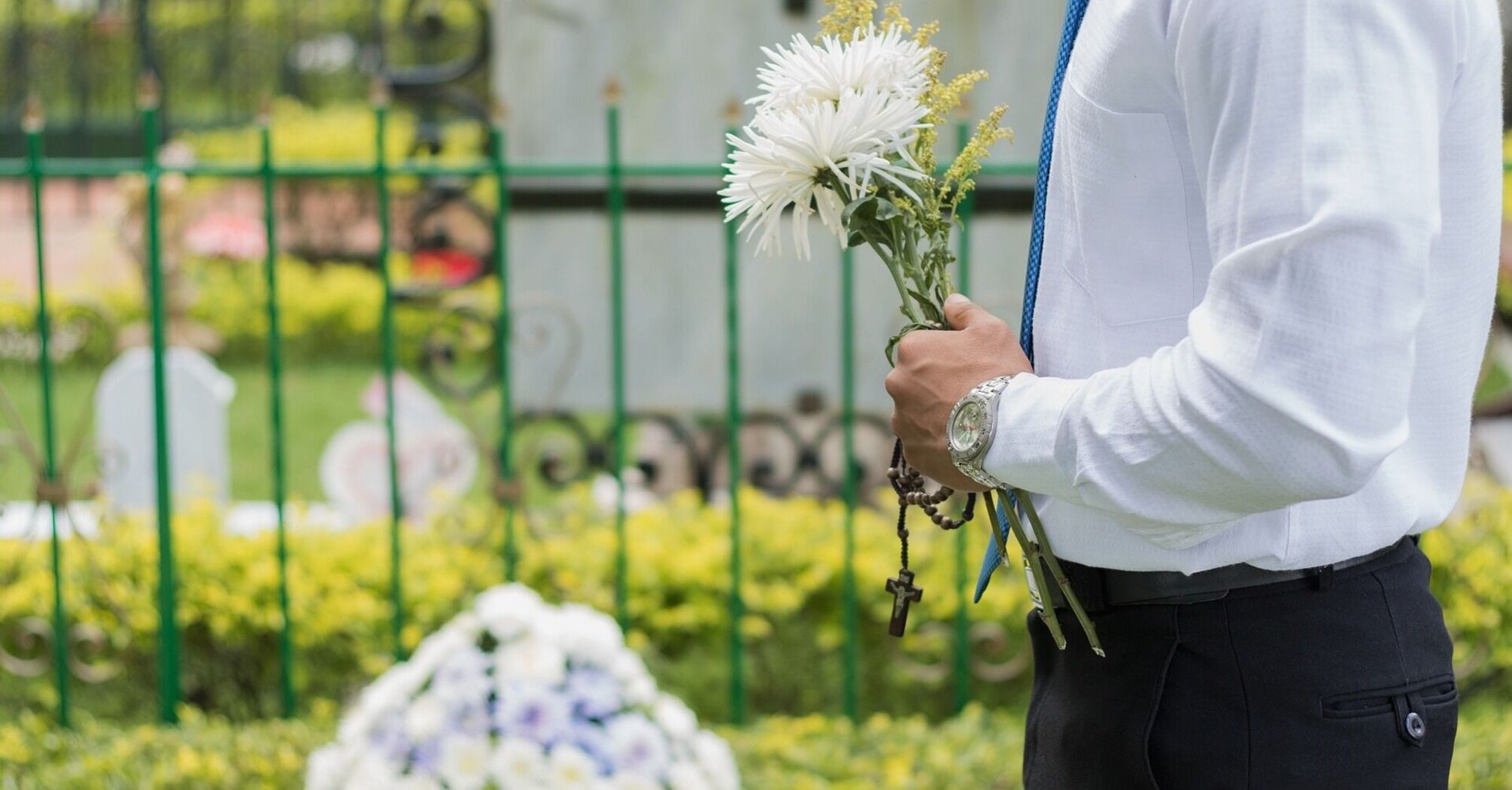 A man stands at the cemetery holding flowers