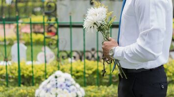 A man stands at the cemetery holding flowers